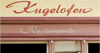 Terracottafarbener Schriftzug "Kugelofen" auf dem gelben Gebäude des Restraurants