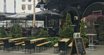 Bierbänke und Biertische vor den großen Holzfässern mit Begrünung dazwischen