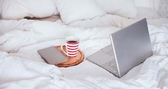 Bett mit darauf stehendem Laptop und einer Kaffeetasse
