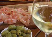 Olives, raw ham and cheese on a wodden plate and a glas whitewine